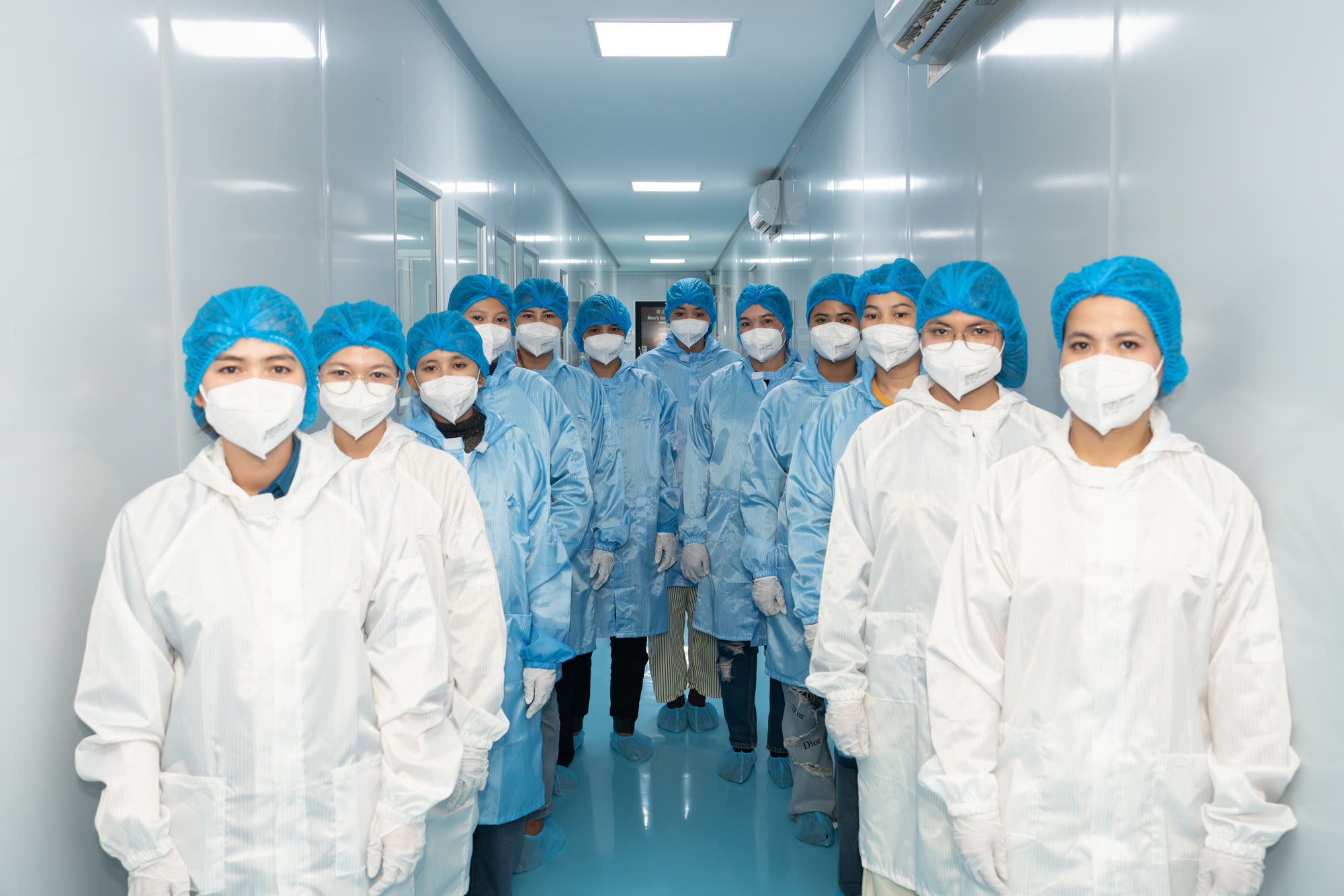 NIS NEST production team in full PPE in a factory corridor, Cambodia